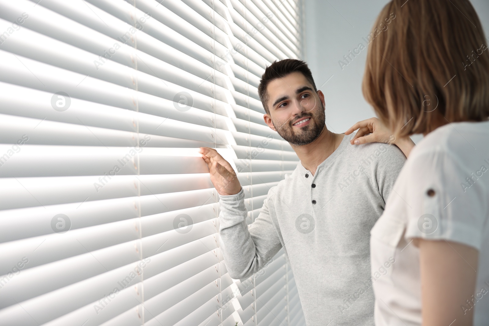 Photo of Young couple near window blinds at home, space for text