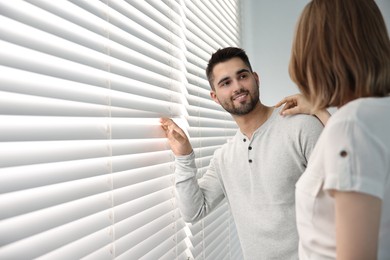 Young couple near window blinds at home, space for text