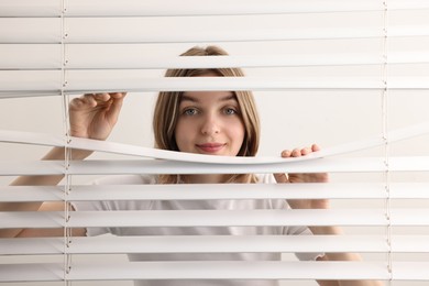 Photo of Young woman looking through window blinds on white background