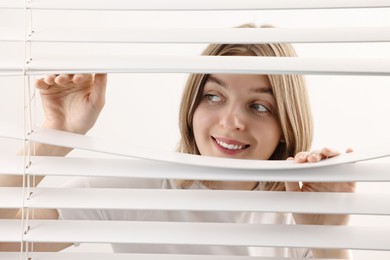 Photo of Young woman looking through window blinds on white background