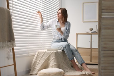 Woman using phone near window blinds at home