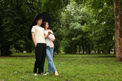 Photo of International dating. Lovely young couple with umbrella spending time together in park, space for text