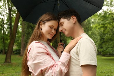 Photo of International dating. Lovely young couple with umbrella spending time together in park