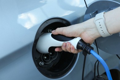 Photo of Woman inserting plug into electric car socket at charging station outdoors, closeup