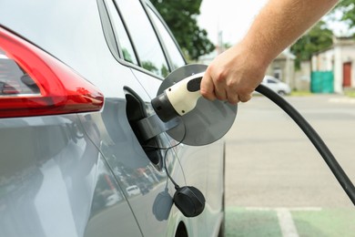 Photo of Man inserting plug into electric car socket at charging station outdoors, closeup