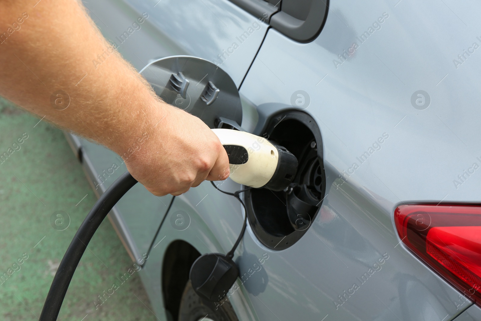 Photo of Man inserting plug into electric car socket at charging station outdoors, closeup