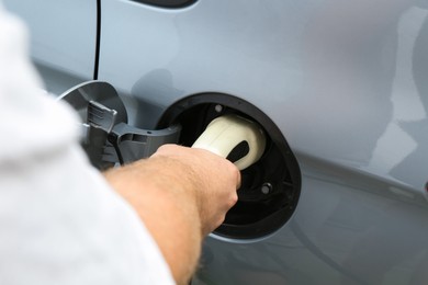 Photo of Man inserting plug into electric car socket at charging station outdoors, closeup