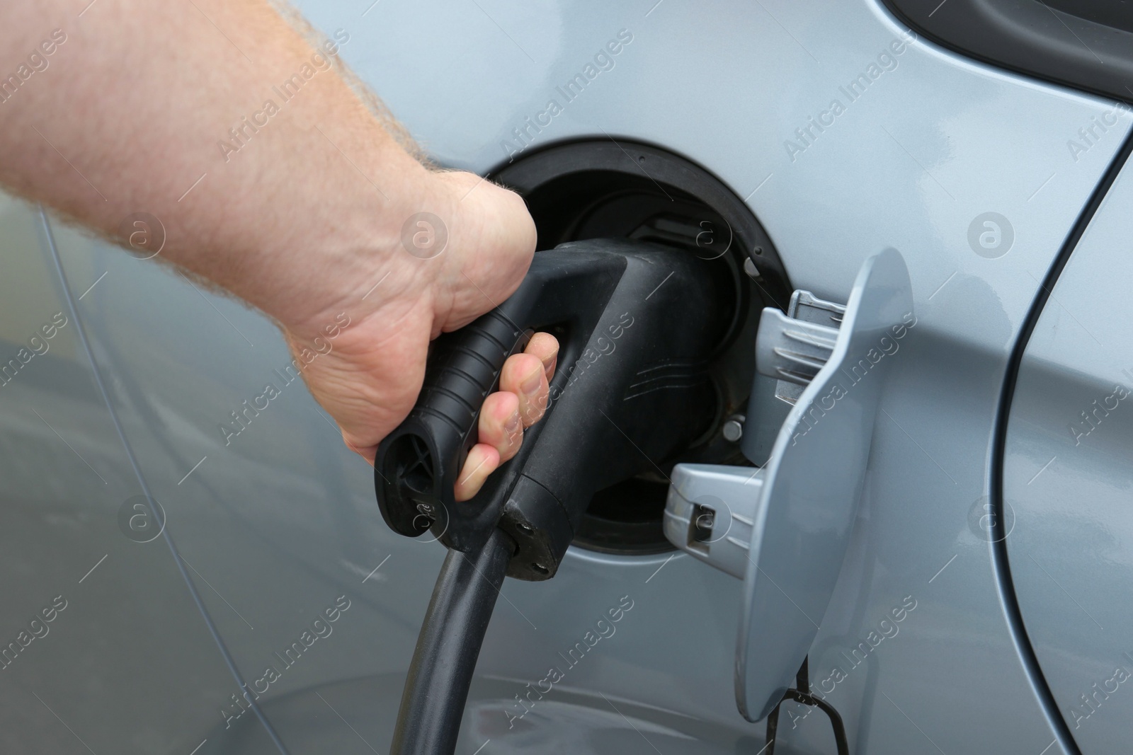 Photo of Man inserting plug into electric car socket at charging station outdoors, closeup