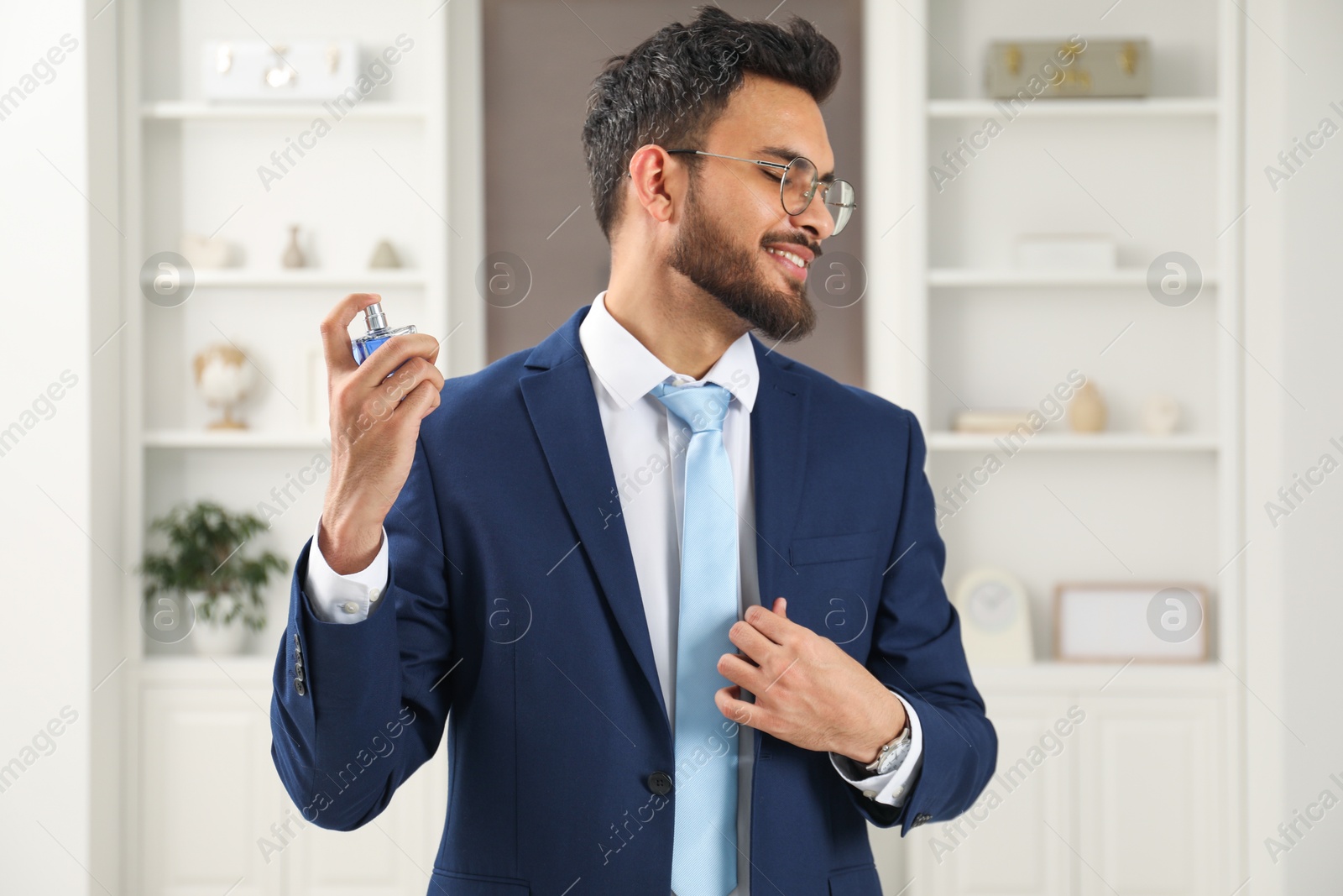 Photo of Attractive young man spraying luxury perfume indoors