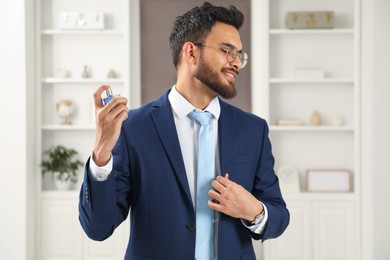 Attractive young man spraying luxury perfume indoors