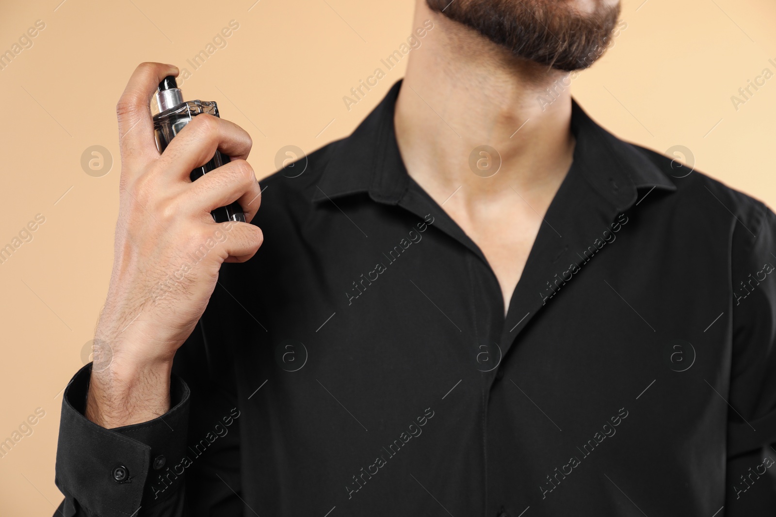 Photo of Man spraying luxury perfume on beige background, closeup