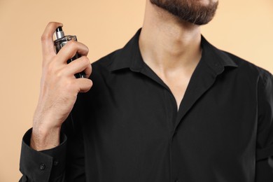 Man spraying luxury perfume on beige background, closeup