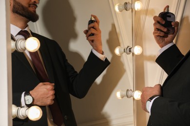 Man spraying luxury perfume near mirror indoors, closeup