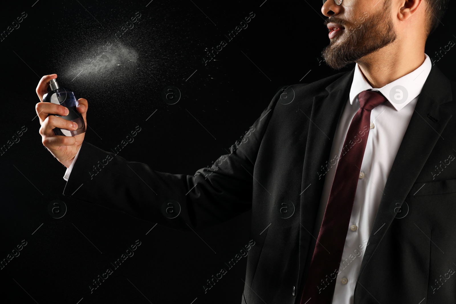 Photo of Man spraying luxury perfume on dark background, closeup