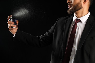 Man spraying luxury perfume on dark background, closeup