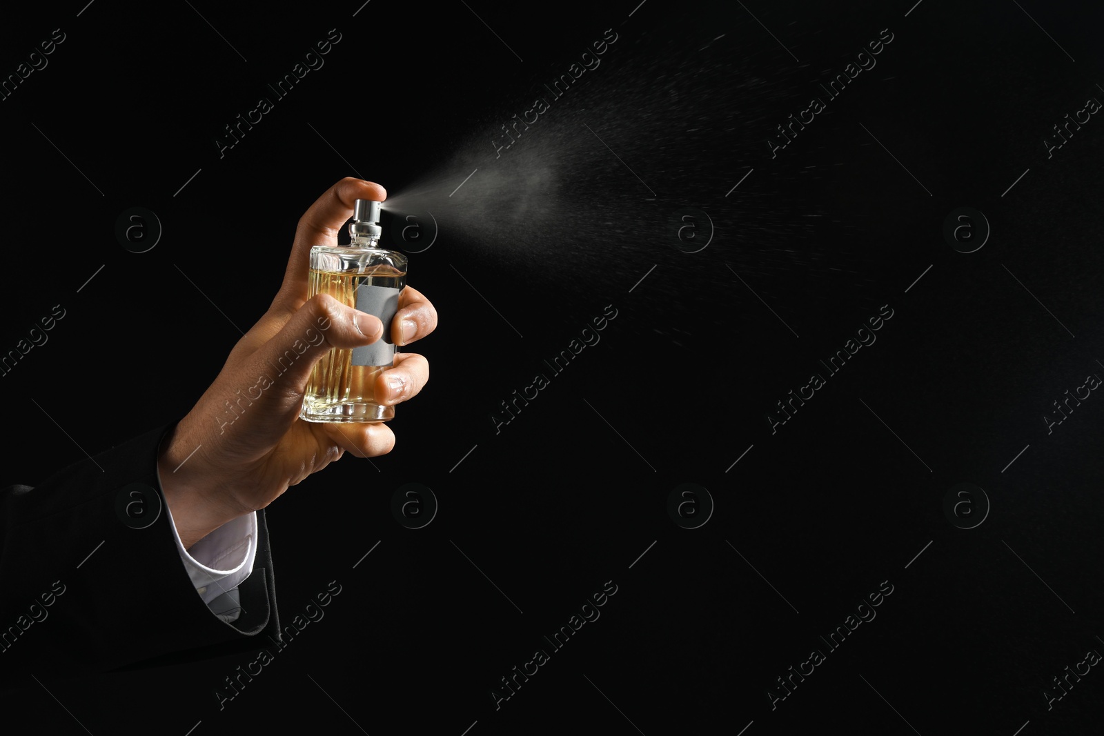 Photo of Man spraying luxury perfume on dark background, closeup. Space for text