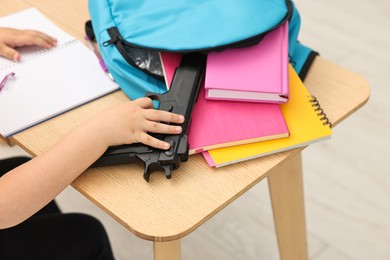 Child taking gun out of backpack at desk in classroom, closeup. School shooting