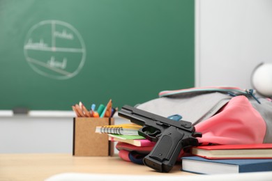 Photo of School stationery, gun and backpack on desk in classroom