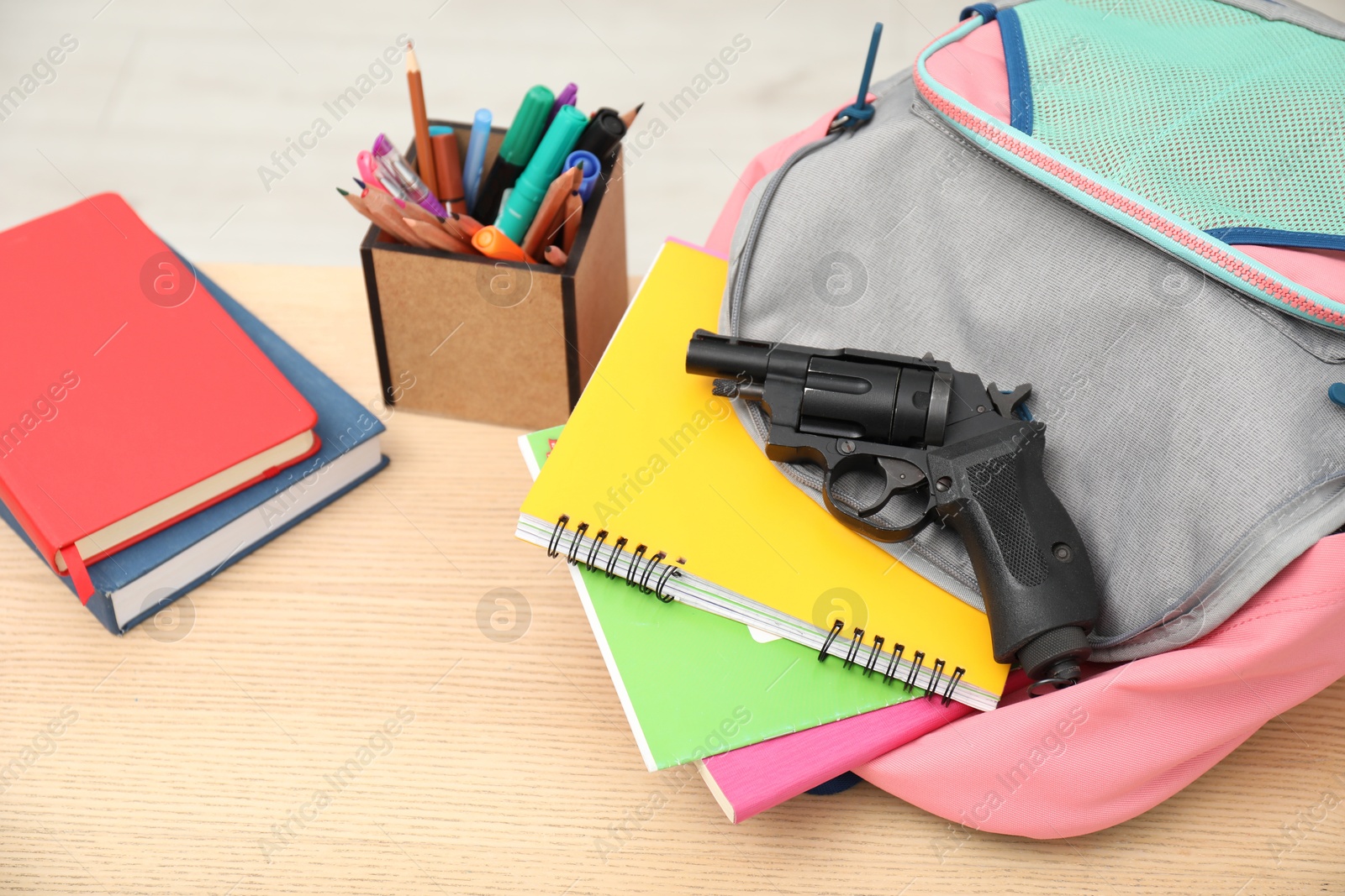 Photo of School stationery and gun on wooden desk, closeup