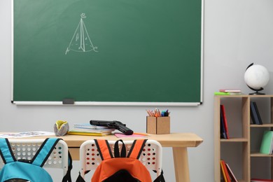 Photo of School stationery and gun on desk in classroom