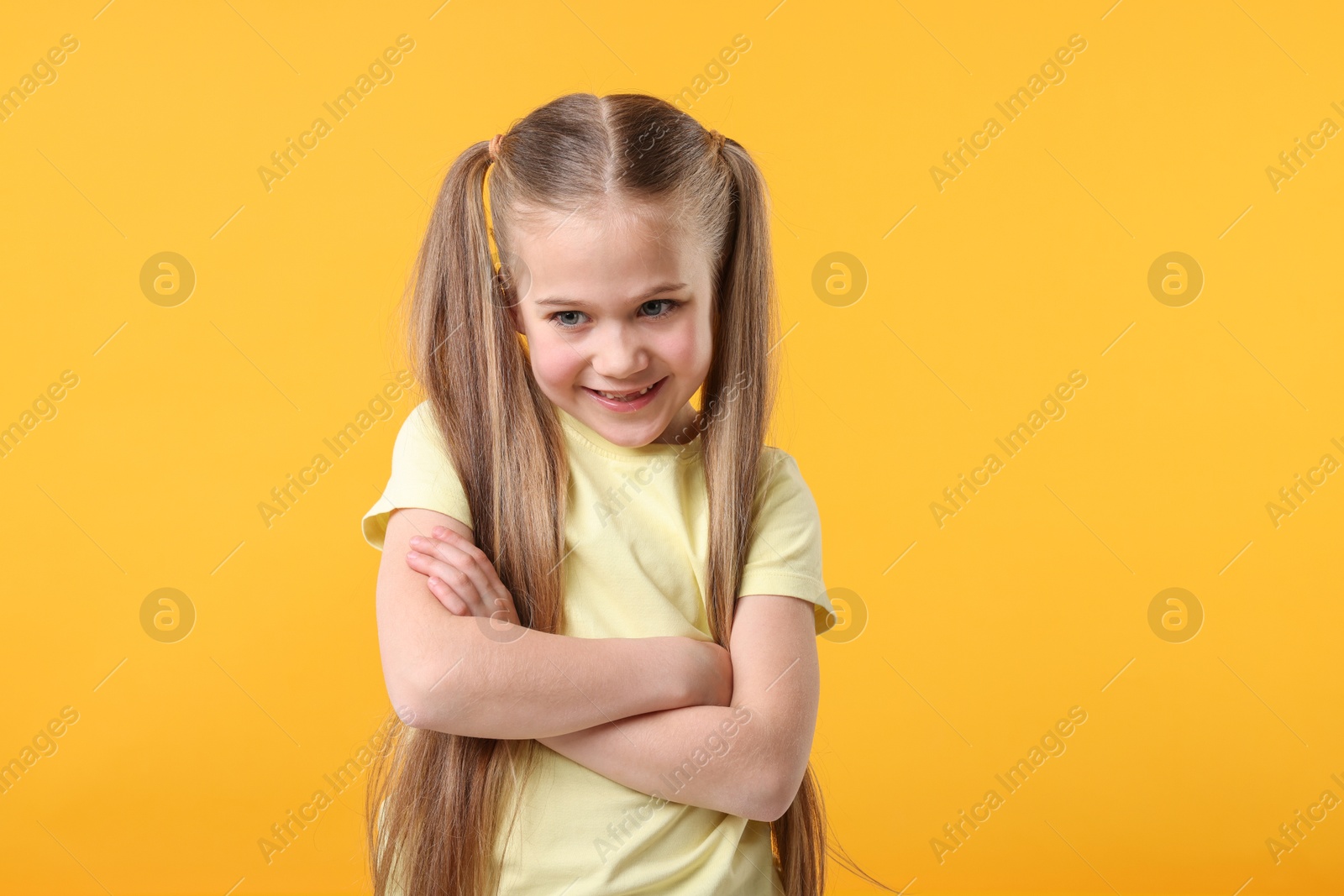 Photo of Portrait of cute little girl with crossed arms on orange background