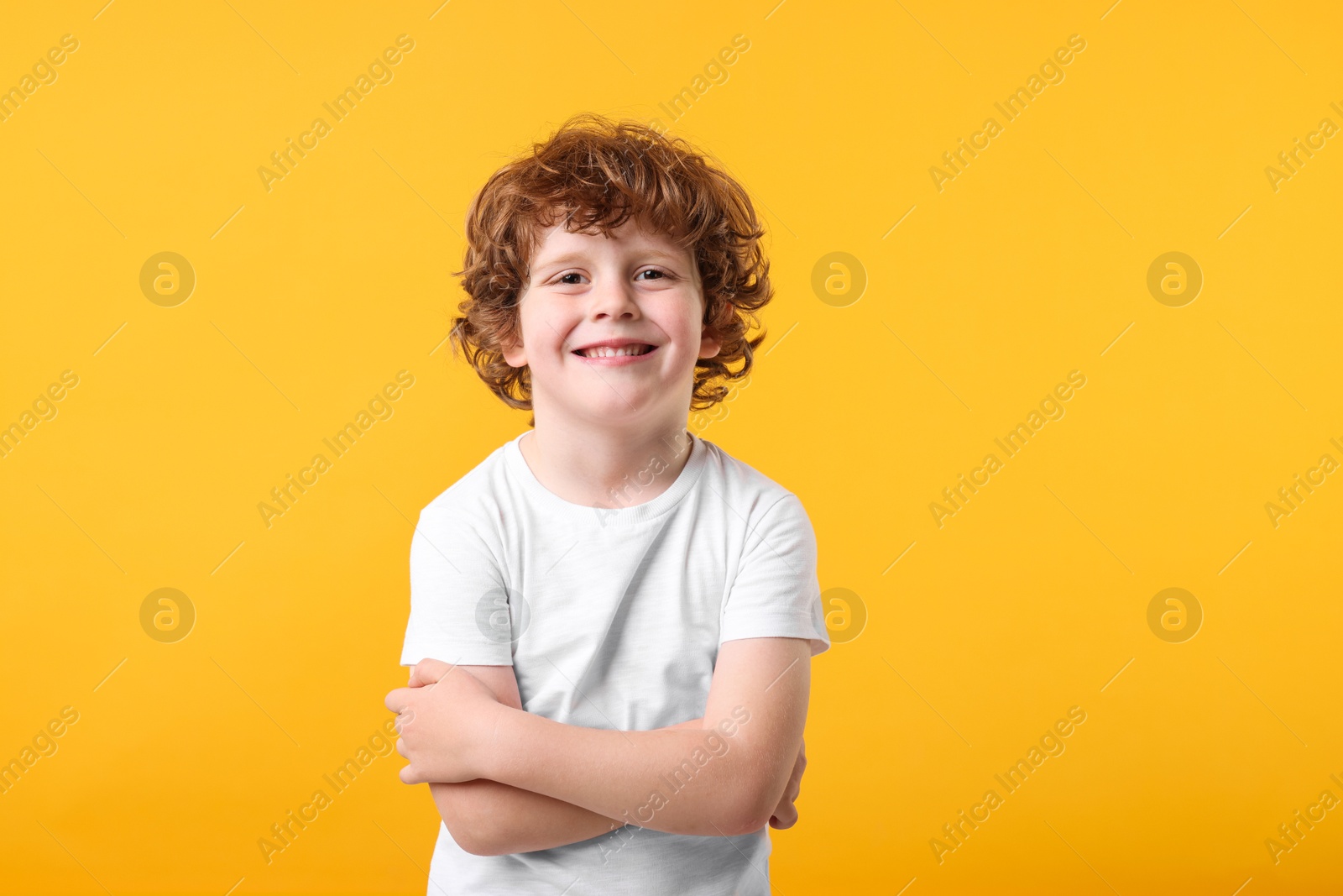 Photo of Portrait of cute little boy with crossed arms on orange background