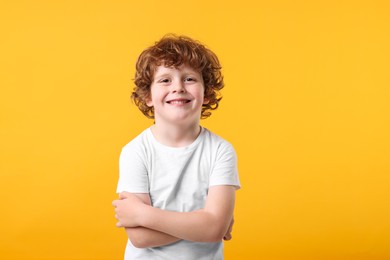 Photo of Portrait of cute little boy with crossed arms on orange background