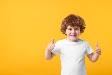 Photo of Cute little boy showing thumbs up on orange background, space for text