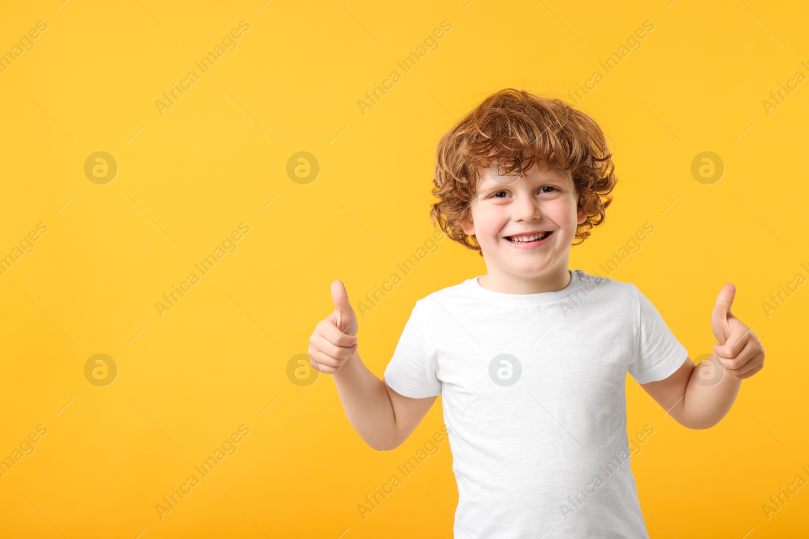Photo of Cute little boy showing thumbs up on orange background, space for text