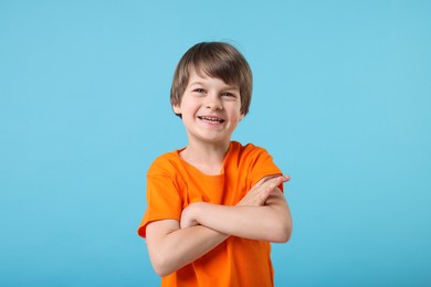Photo of Portrait of cute little boy with crossed arms on light blue background