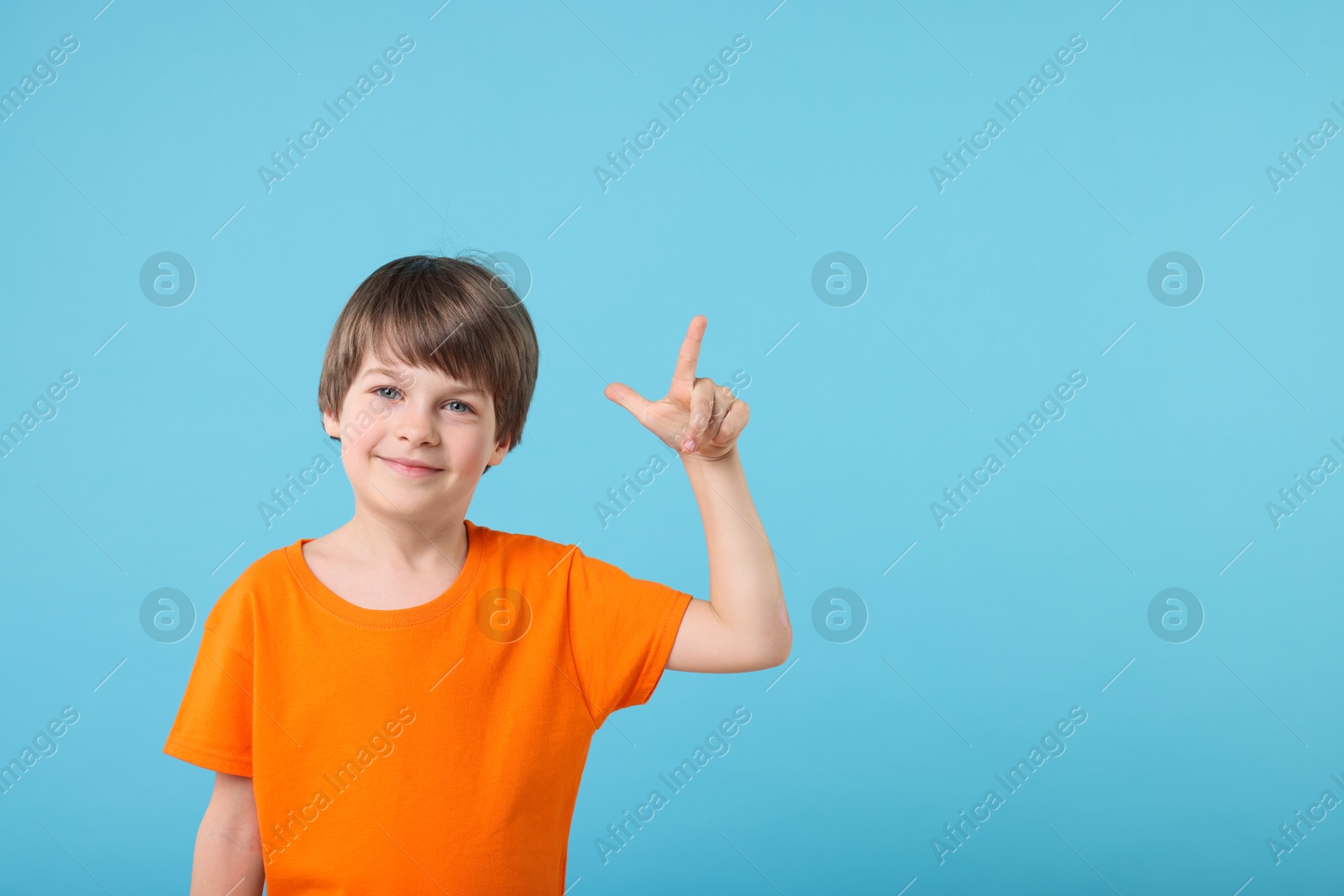 Photo of Cute little boy pointing at something on light blue background, space for text