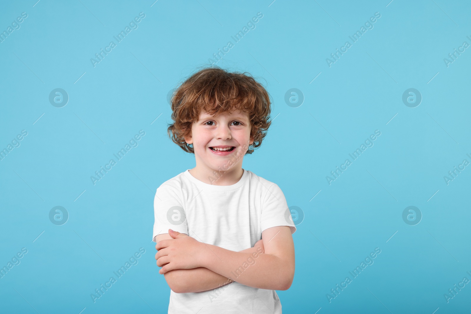 Photo of Portrait of cute little boy with crossed arms on light blue background