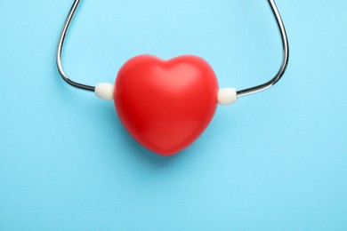 Stethoscope and red heart on light blue background, top view