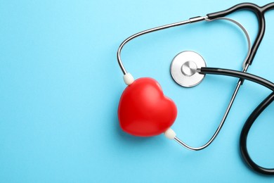 Photo of Stethoscope and red heart on light blue background, top view. Space for text