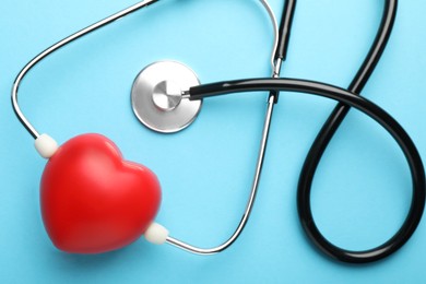 Photo of Stethoscope and red heart on light blue background, top view