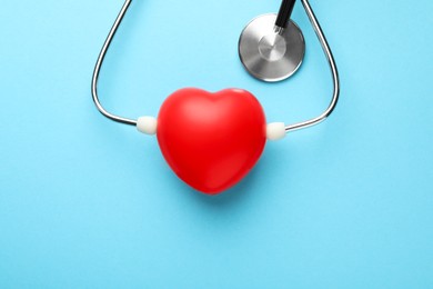 Stethoscope and red heart on light blue background, top view