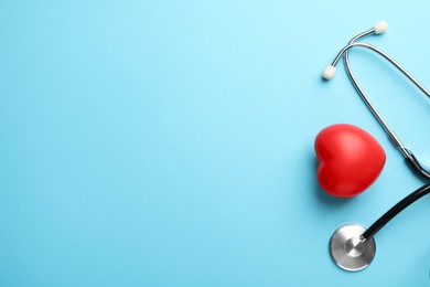 Stethoscope and red heart on light blue background, top view. Space for text