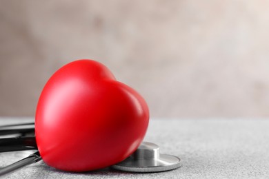 Photo of Stethoscope and red heart on grey stone table, closeup. Space for text