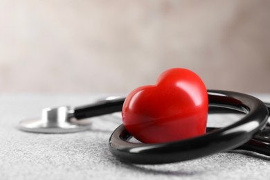 Photo of Stethoscope and red heart on grey stone table, closeup. Space for text