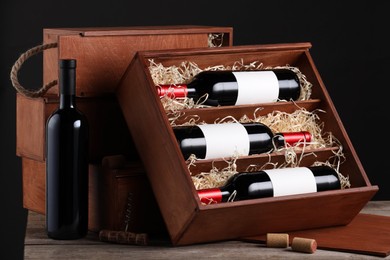 Box with wine bottles on wooden table against black background