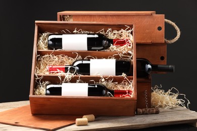 Box with wine bottles on wooden table against black background