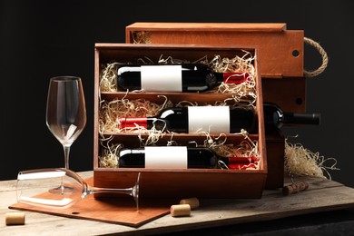 Box with wine bottles, corks and glasses on wooden table against black background