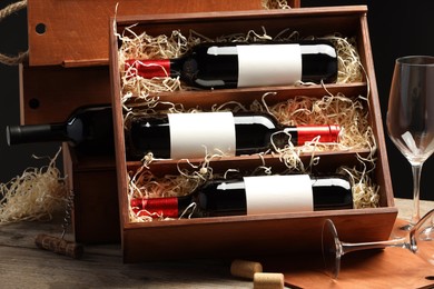 Box with wine bottles, corks and glasses on wooden table against black background