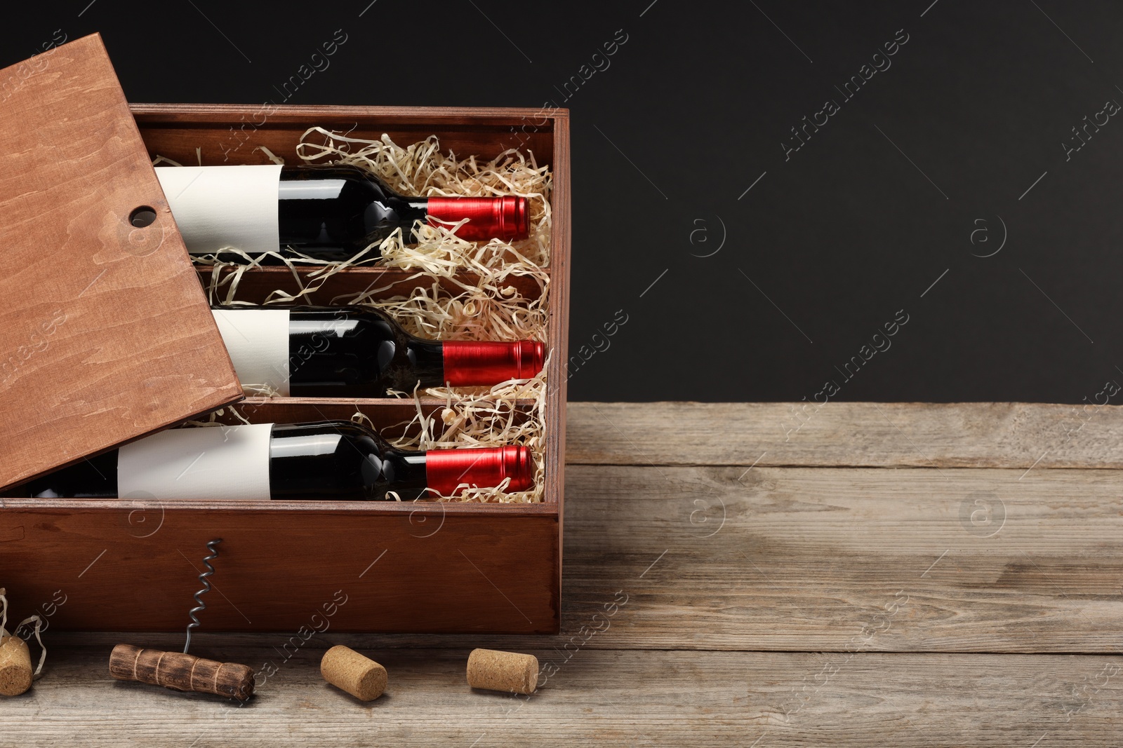 Photo of Box with wine bottles, corkscrew and corks on wooden table against black background. Space for text