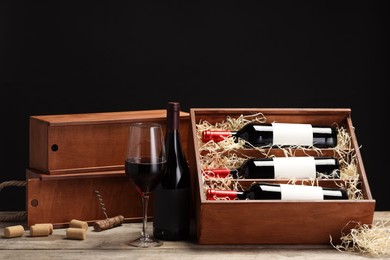 Box with wine bottles, glass, corks and corkscrew on wooden table against black background