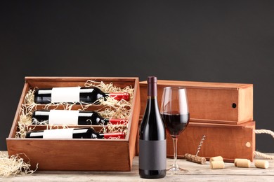 Box with wine bottles, glass, corks and corkscrew on wooden table against black background