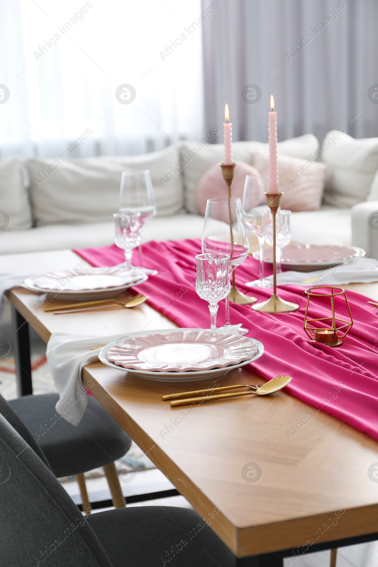 Photo of Beautiful table setting with burning candles and pink accent in dining room