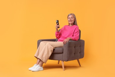 Photo of Senior woman with phone on armchair against orange background