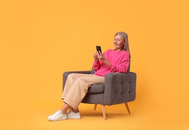 Senior woman with phone on armchair against orange background