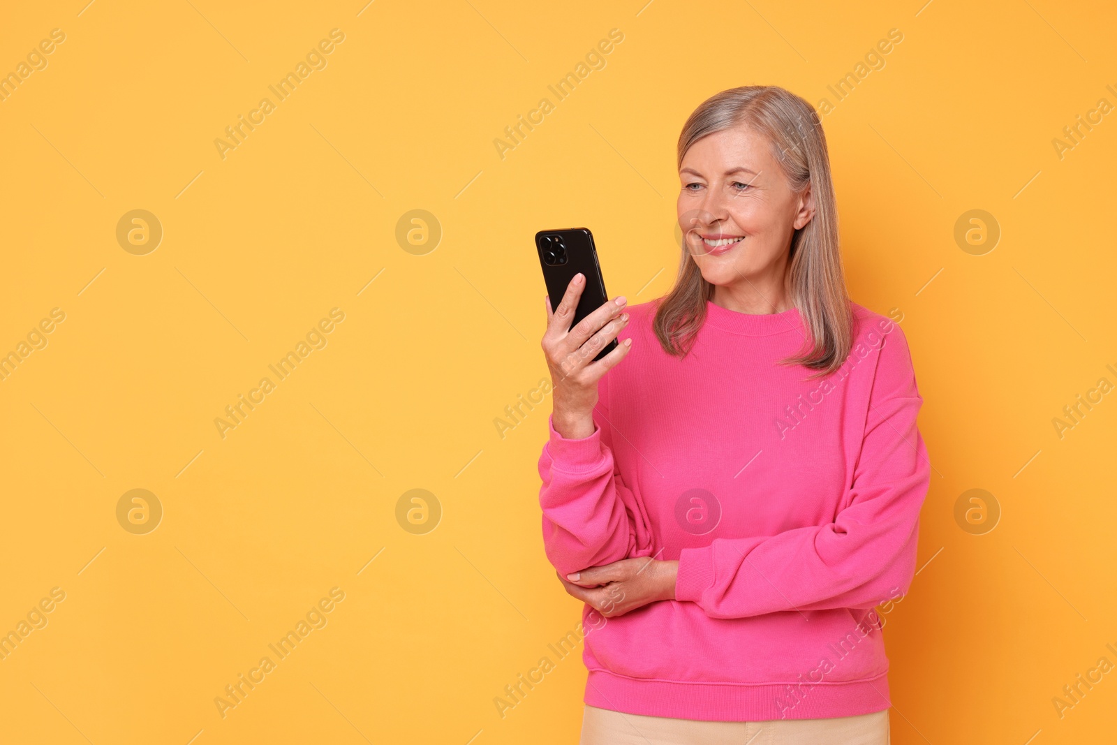 Photo of Senior woman with phone on orange background, space for text